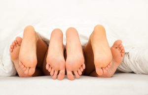 Three pairs of feet in bed